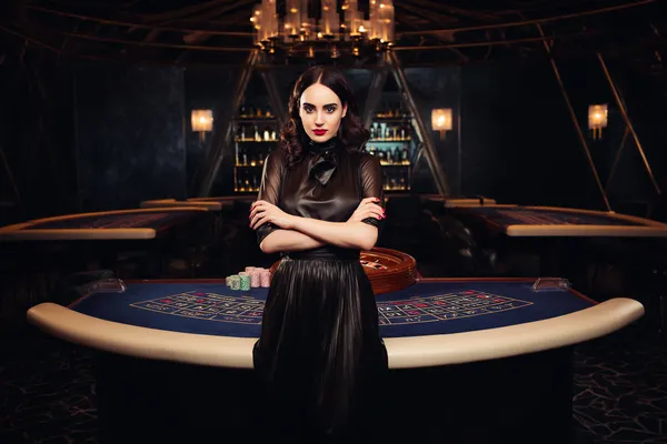 Một cô gái trong bộ váy xanh sang trọng đứng cạnh vòng roulette, gợi lên bầu không khí casino cao cấp của F16886.